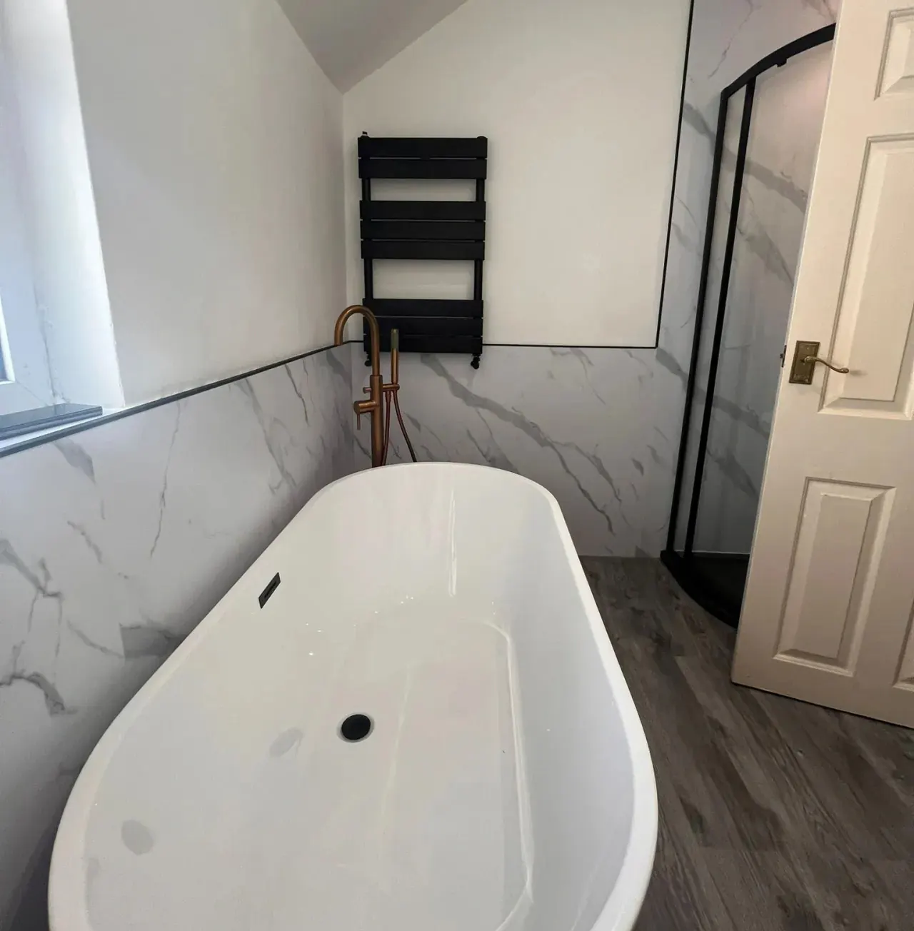 Plumbing services in Cardiff: freestanding bath and black towel radiator installed in a loft bathroom