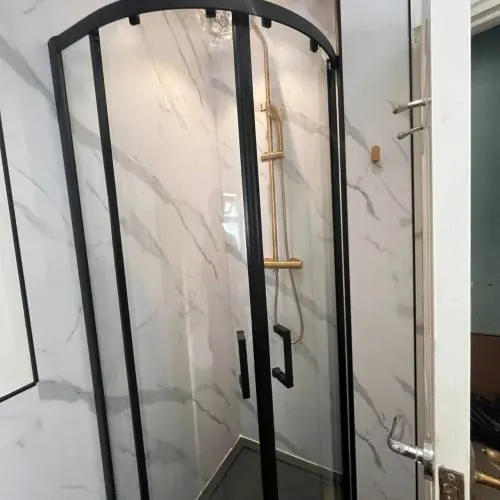 Black-framed quadrant shower enclosure with marble-effect wall panels in a Cardiff bathroom