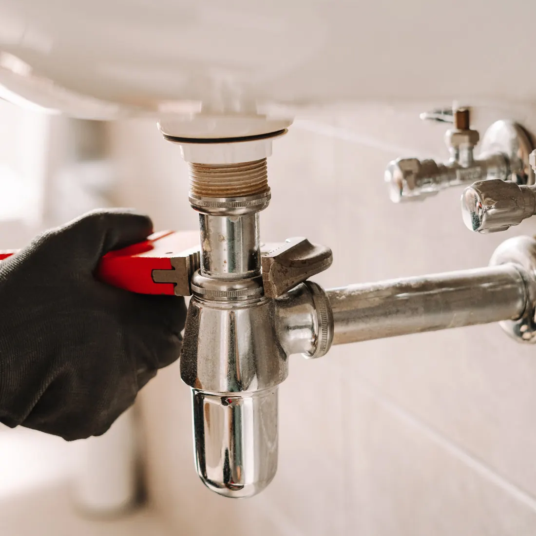 General plumbing by a plumber in Cardiff tightening a chrome basin trap